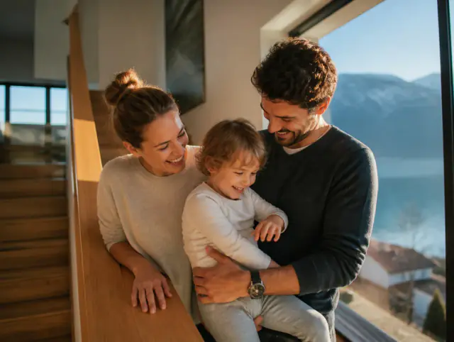 Glückliche Familie mit Kind lacht gemeinsam an einem Treppengeländer aus Holz