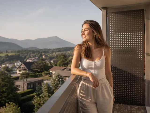 Balkongeländer mit Lochblech – lächelnde Frau blickt zum Horizont Lächelnde Frau geniesst den Ausblick an einem Balkongeländer mit Lochblech
