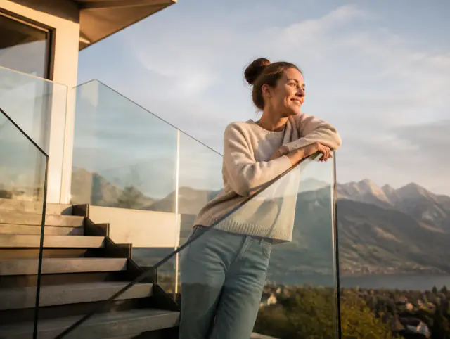 Glasgeländer aussen – lächelnde Frau blickt zum Horizont Lächelnde Frau geniesst den Ausblick an einem Glasgeländer aussen